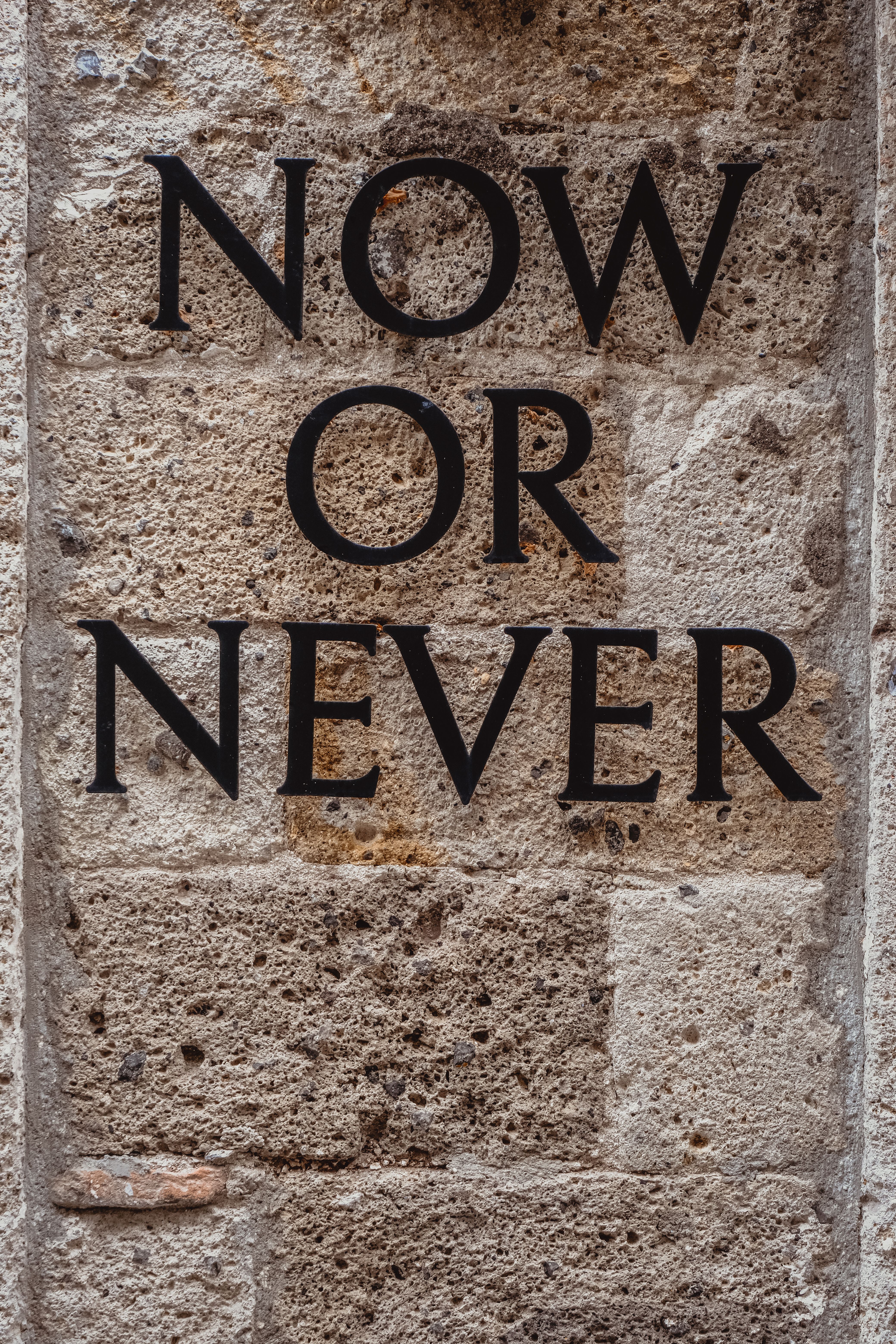 Close-up of 'Now or Never' text on rustic stone wall, motivational concept.