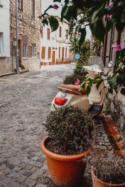 Free A quaint cobblestone alley in a European town featuring a parked scooter and lush greenery. Stock Photo