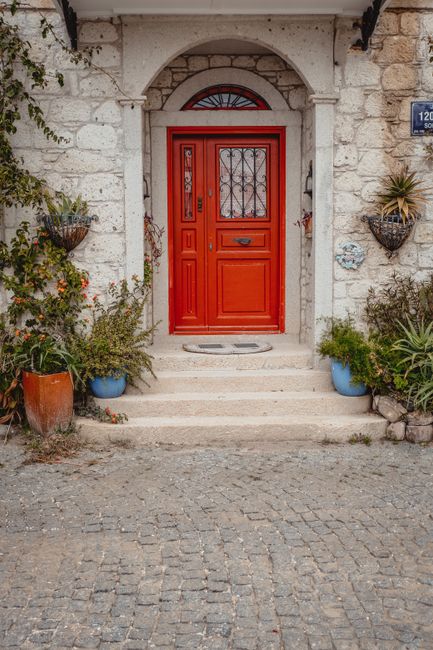 Rustic entrance featuring a vibrant red door set in a stone wall, surrounded by lush plants.