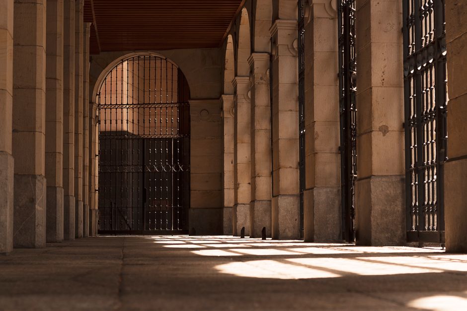 Encantador corredor arqueado con luz solar que entra a través de puertas de hierro y columnas de piedra.