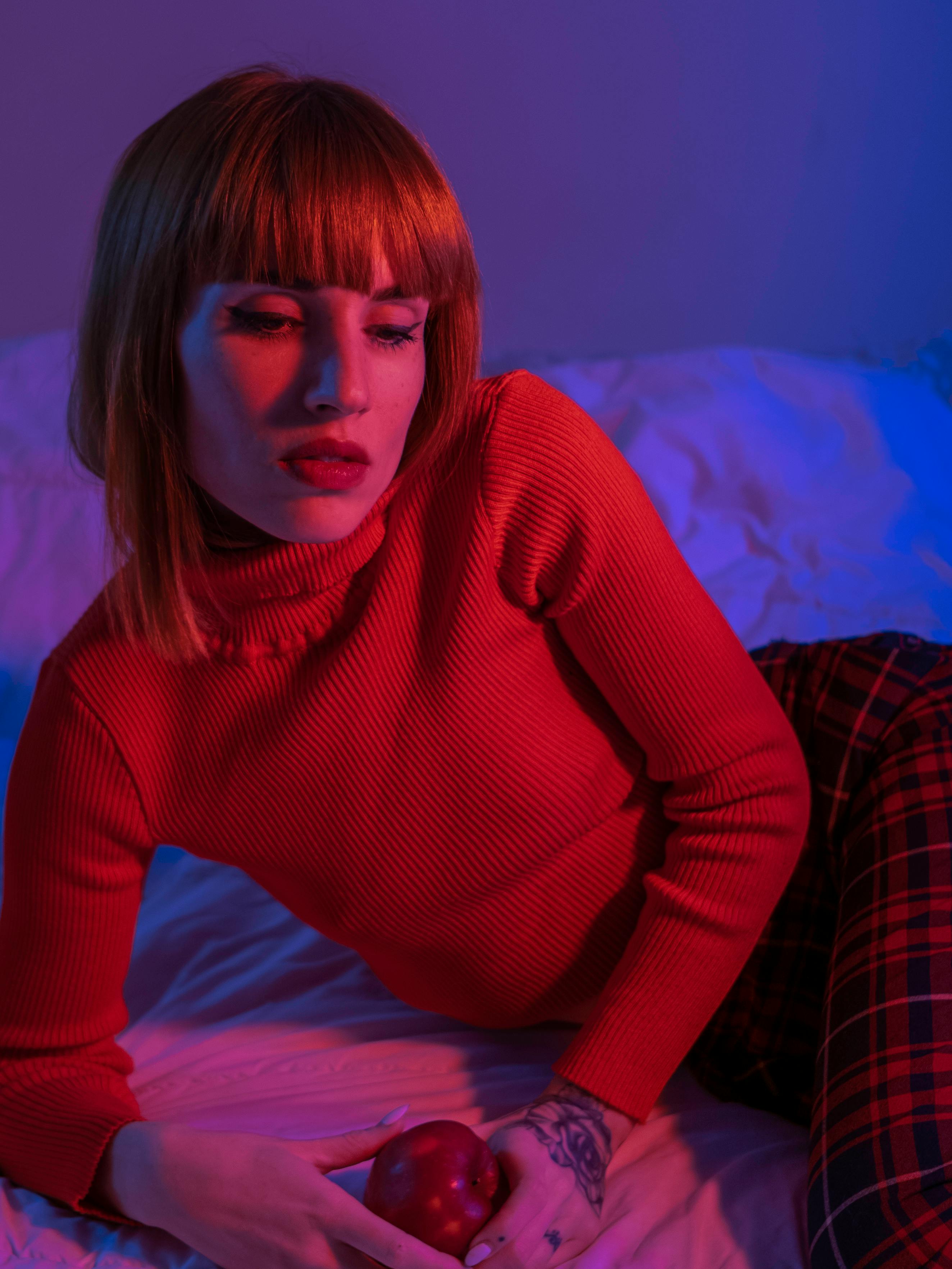 A creative portrait of a woman in red attire under blue lighting, holding an apple.