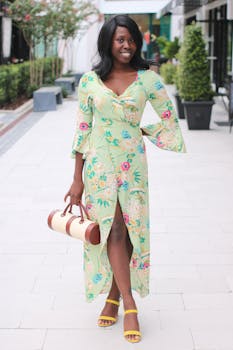 Chic outdoor portrait of a smiling woman in a floral dress, holding a handbag on a city street.