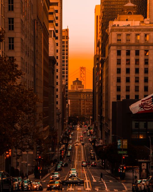 Captivating sunset view of a busy San Francisco street with skyscrapers and distant bridge.