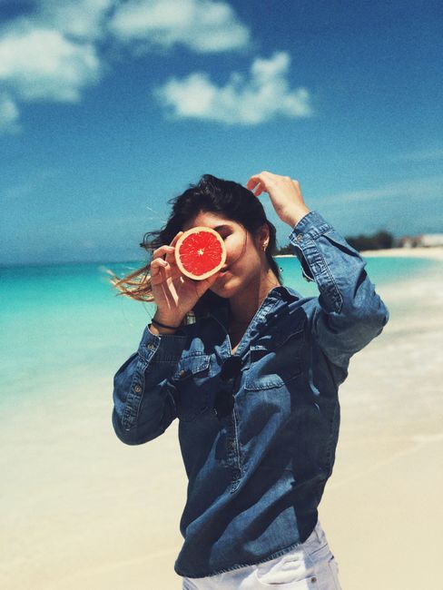 Woman enjoying a sunny day on a tropical Bahamas beach, holding a grapefruit slice.