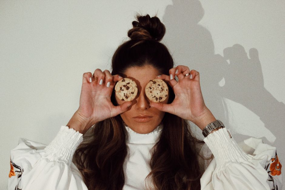 Woman playfully holds chocolate chip cookies over her eyes indoors.