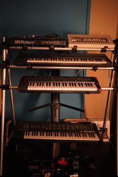 A collection of electronic keyboards and sound equipment arranged on a metal frame in a studio setting.