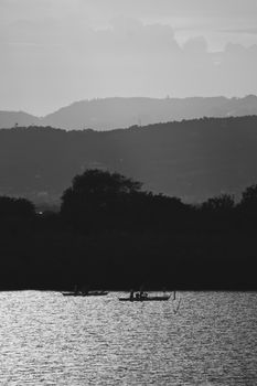 Black and white landscape with boats on a calm lake under scenic hills.