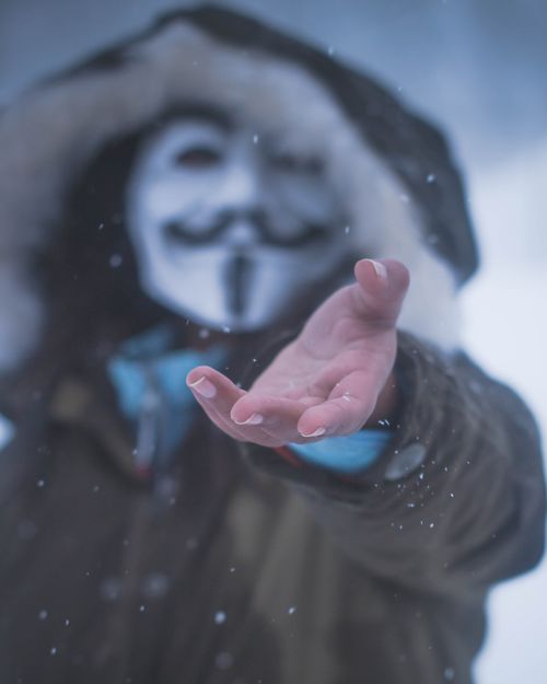 Free A masked figure reaches out amidst falling snow, creating an enigmatic winter scene. Stock Photo