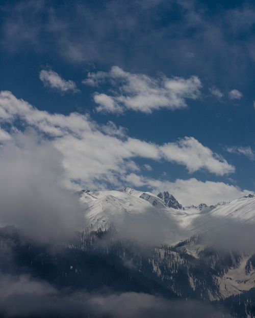 Free Majestic aerial view of snow-covered mountains amidst drifting clouds beneath a deep blue sky. Stock Photo