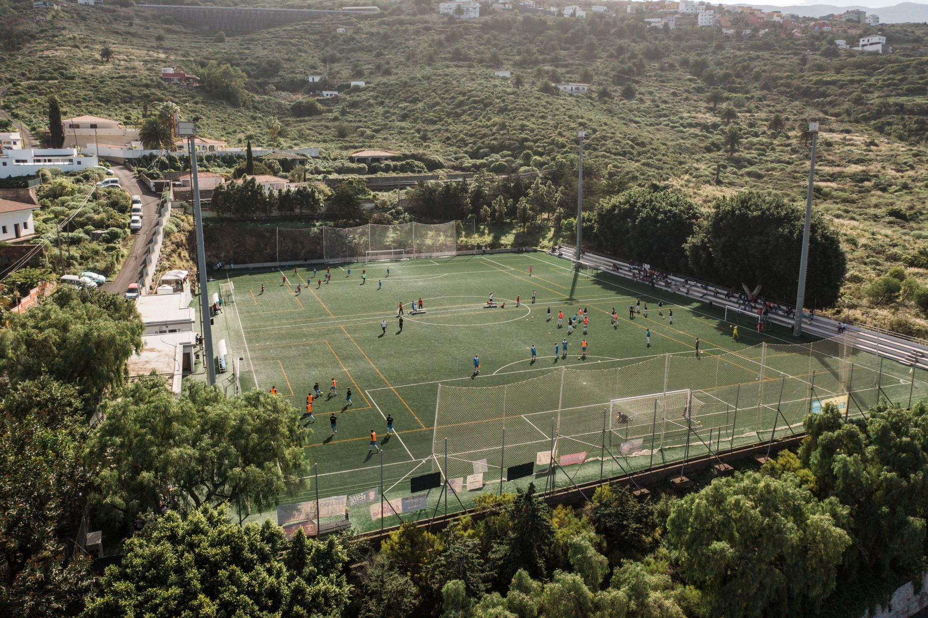 Aerial shot of soccer match on a rural field in El Sauzal, Spain, surrounded by lush greenery.