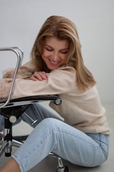 A woman with long blonde hair smiles while sitting on an office chair indoors.