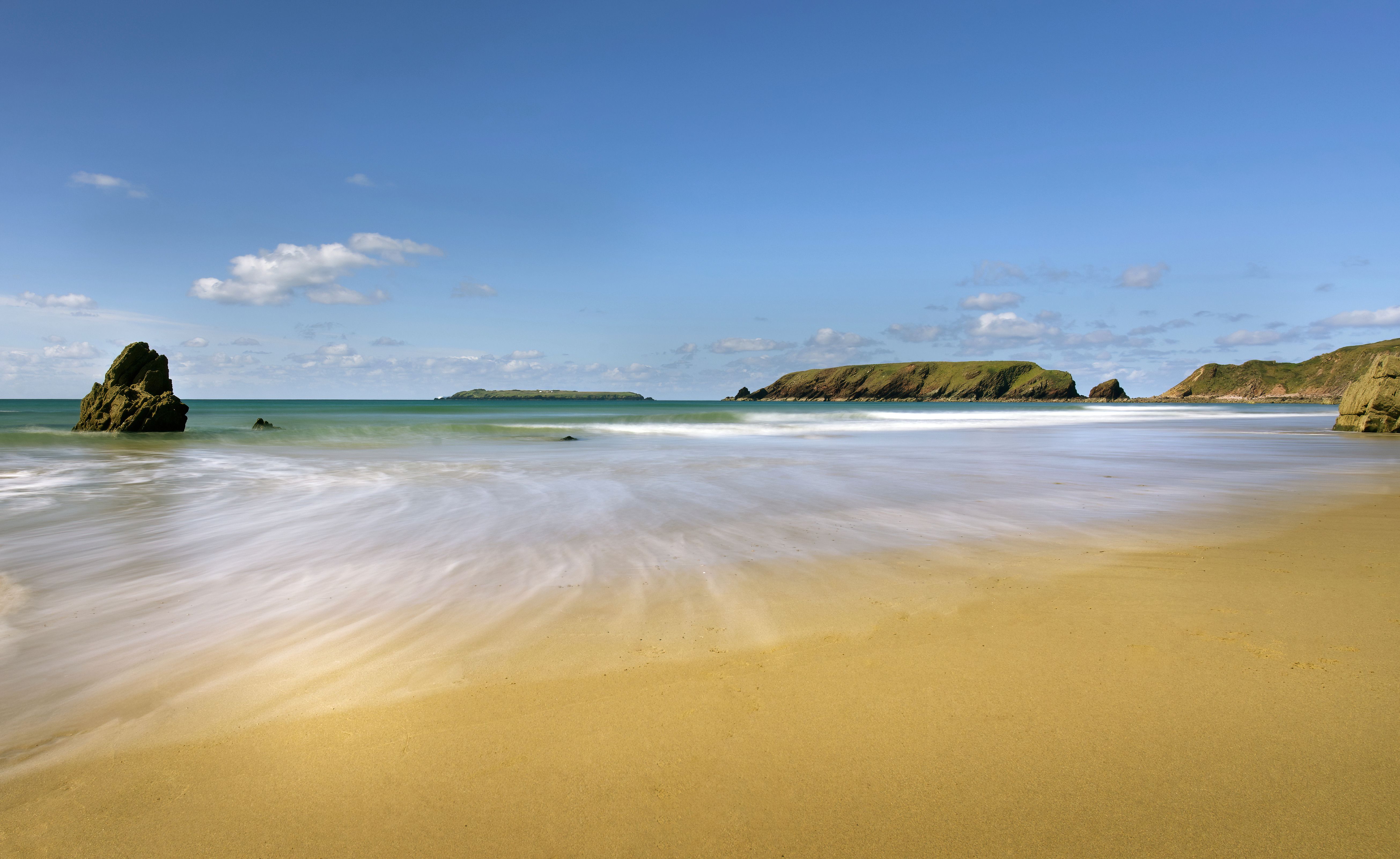 Beautiful Marloes Sands in Wales with waves hitting the sandy shore under a clear blue sky.