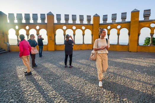 Tourists explore the vibrant yellow walls of a historic castle in Sintra, Portugal, during summer.