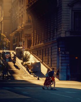 Two pedestrians walking in Buenos Aires at golden hour, with sunlight casting long shadows.