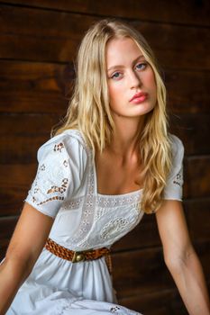 A stylish woman in a white embroidered sundress poses indoors against a wooden backdrop.