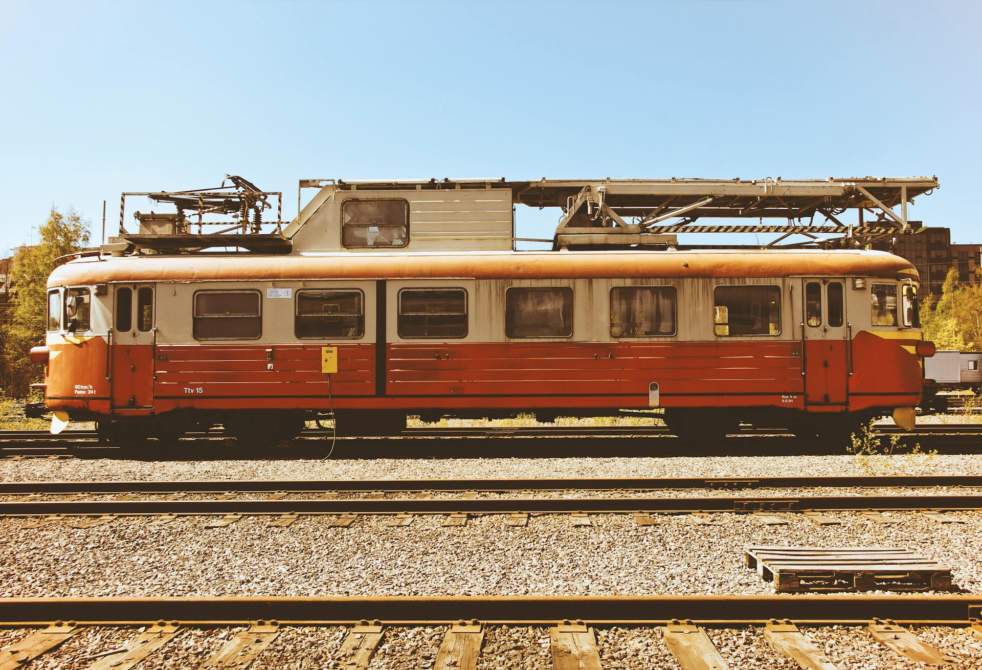 A vintage rusty electric train parked on railway tracks in a sunlit railway yard.