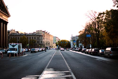 Free A bustling city street lined with cars at sunset, capturing urban life. Stock Photo