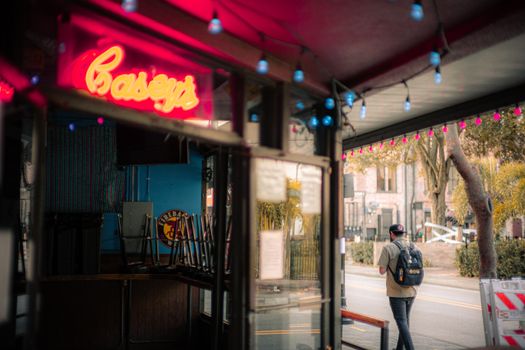 Urban scene with vibrant neon sign and man walking on a city street.