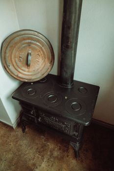 A classic vintage iron stove with a cast iron chimney against a white wall.