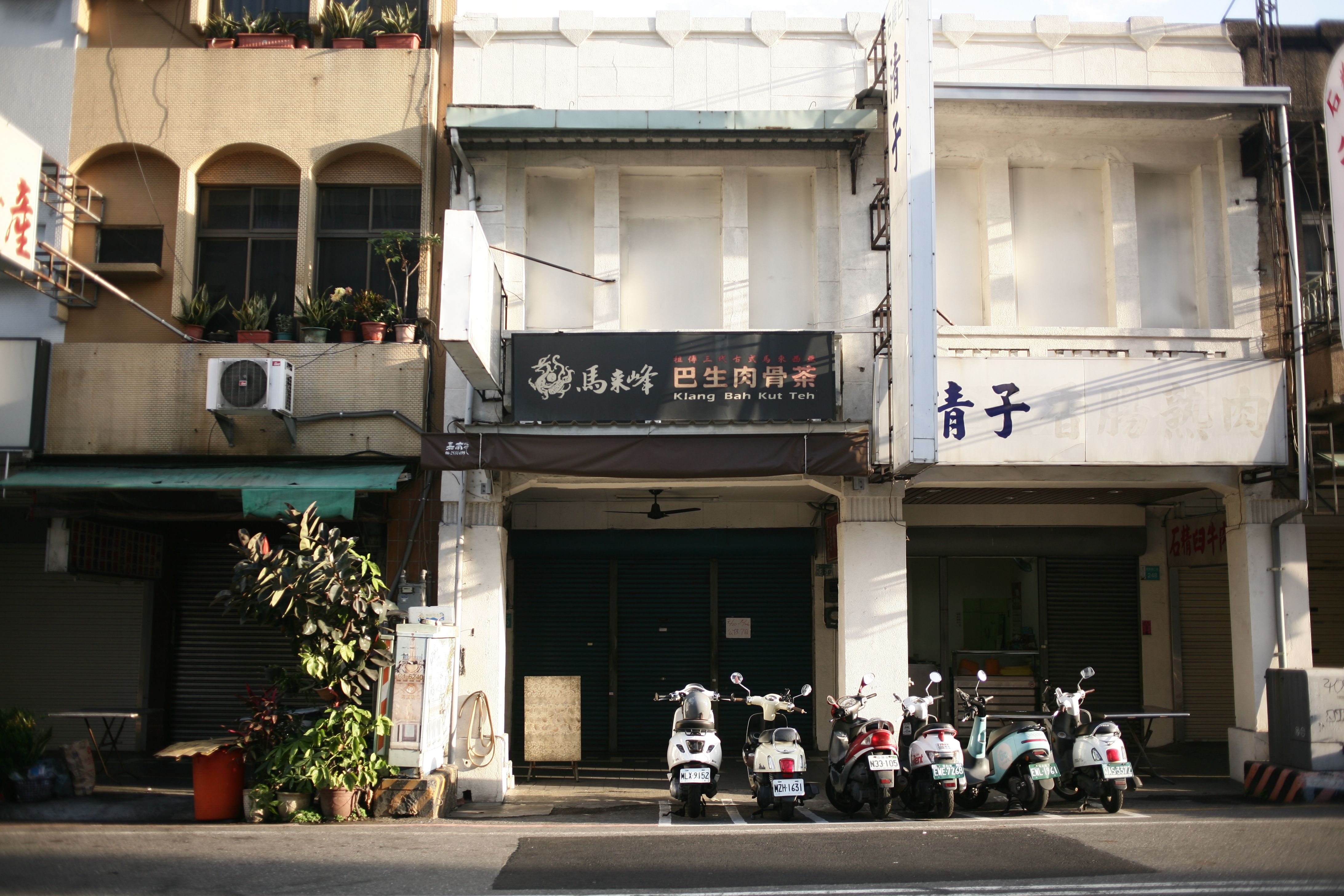 Street view of scooters parked in front of closed shops with Chinese signage in an Asian city.