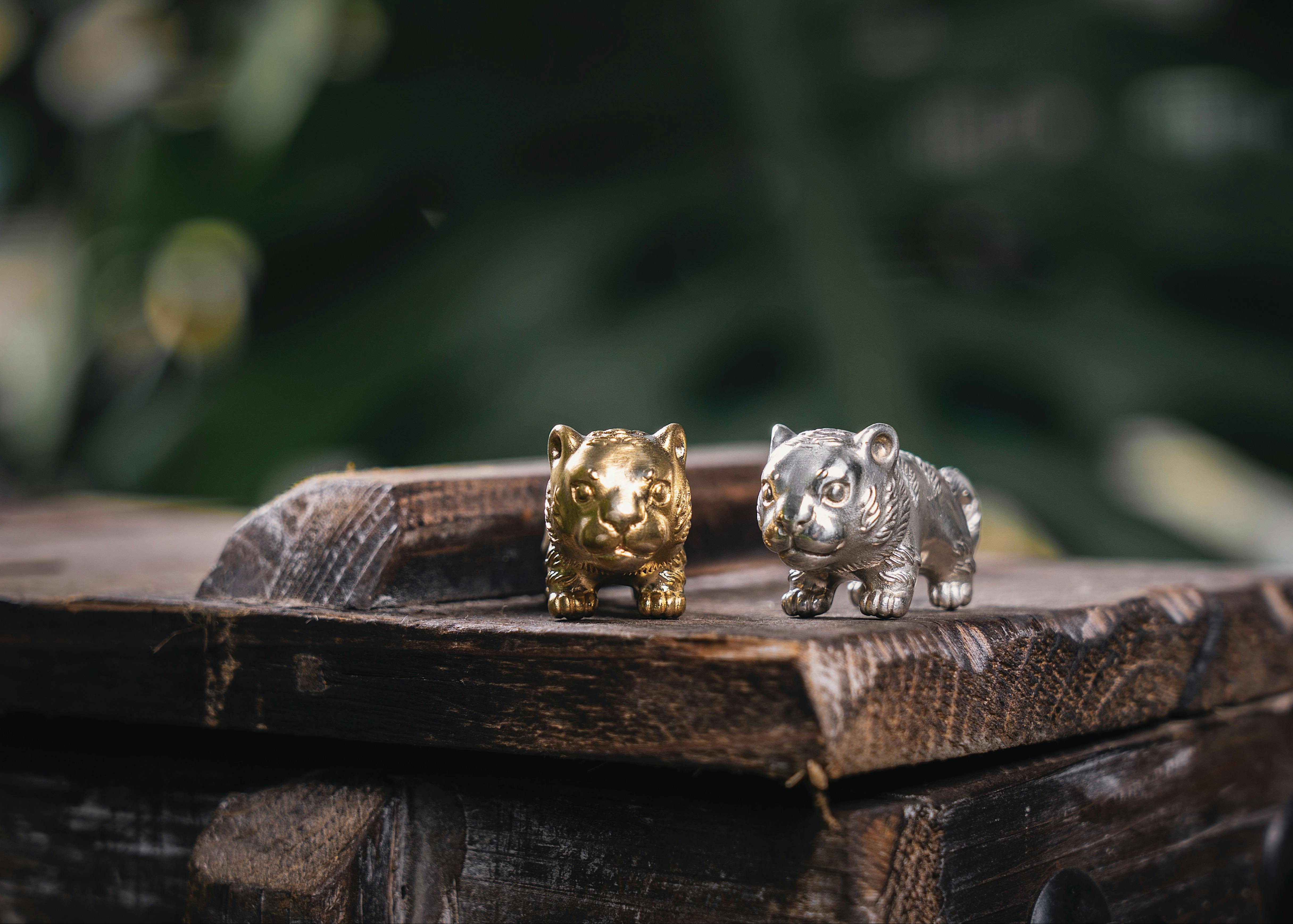 Close-up of golden and silver tiger figurines on wooden table outdoors.