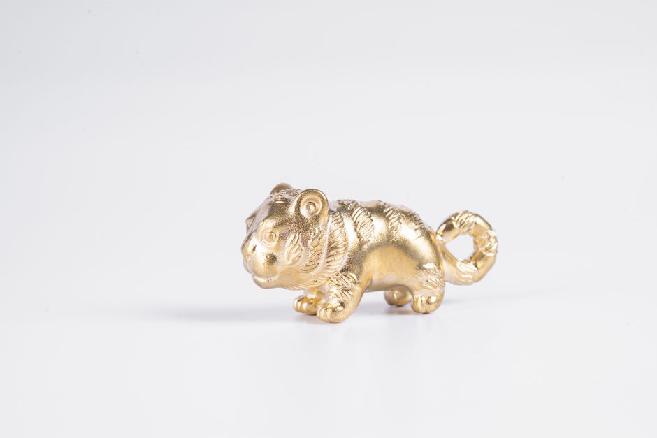 Close-up of a small golden tiger figurine on a white background, showcasing simplicity and elegance.