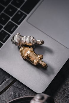 Close-up view of silver and gold animal figurines resting on a laptop. High angle perspective highlighting tech and art fusion.