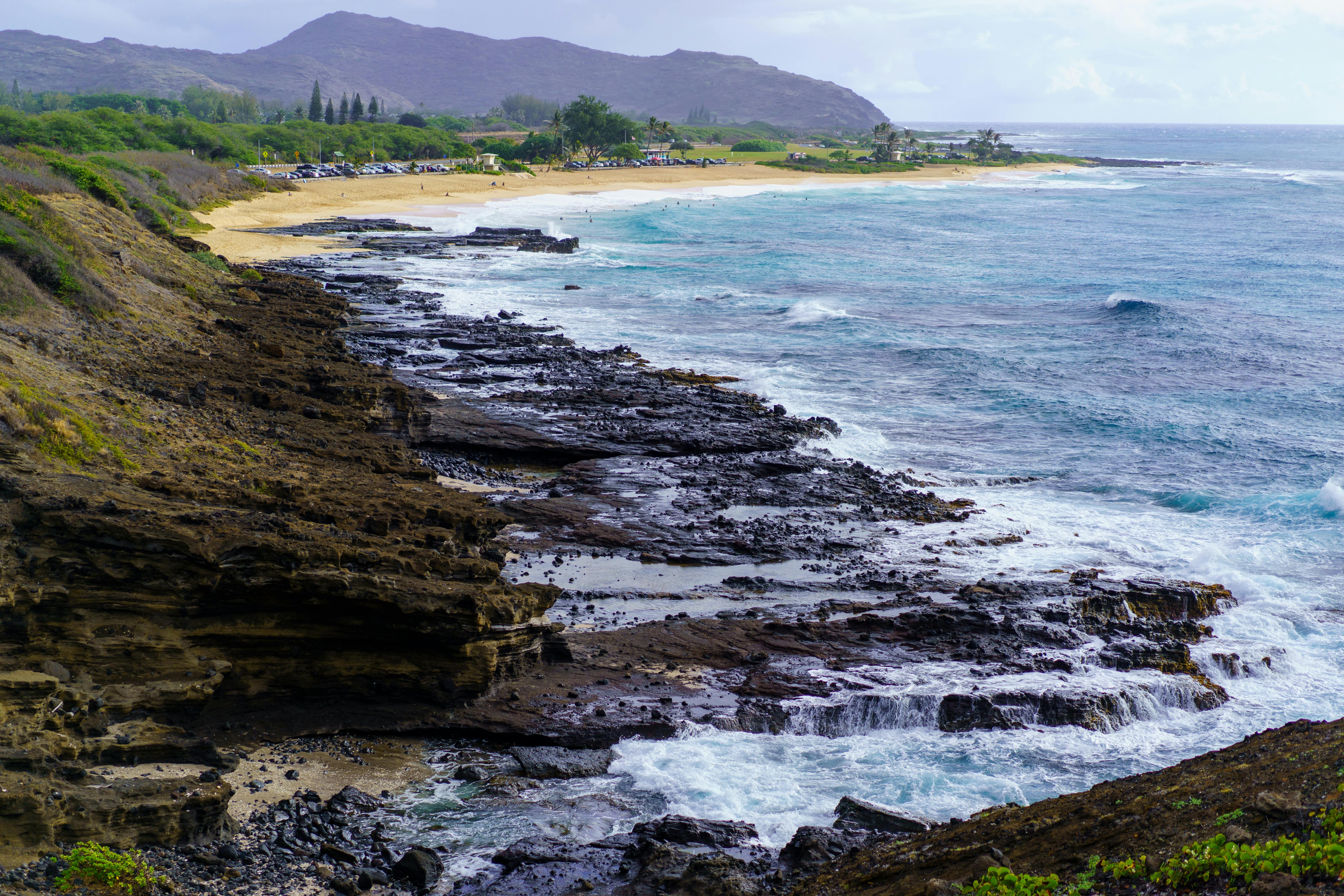Dramatic coastal landscape featuring rocky cliffs and pristine beach with lush green backdrop in Hawaii.
