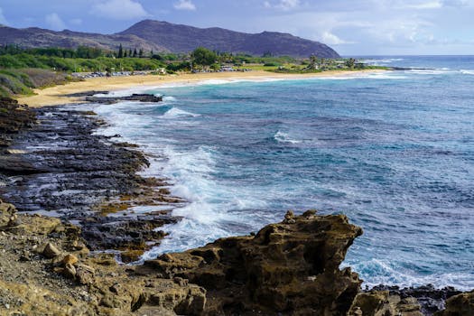 Photo by Cyrill Beautiful view of a beach in Hawaii with rocky coastline and turquoise ocean waves crashing toward the shore.