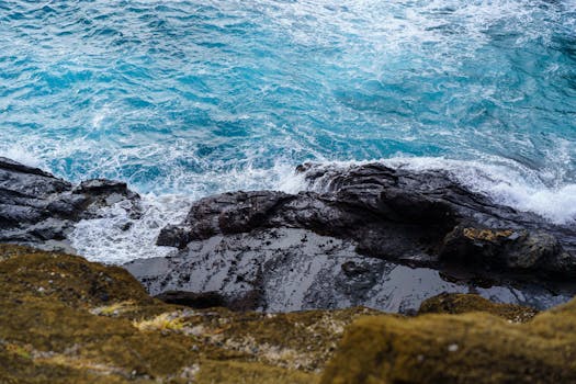 Photo by Cyrill Vibrant blue ocean waves crash on sunlit rocky shores, creating foam and splashes.