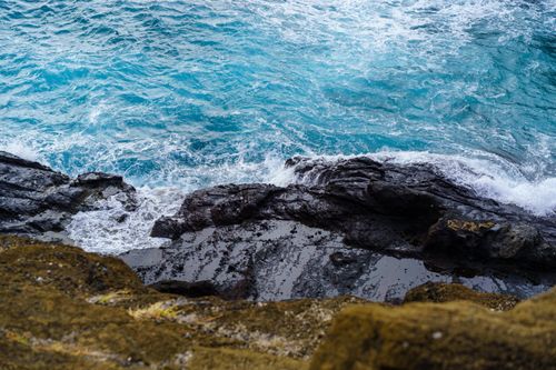 Free Vibrant blue ocean waves crash on sunlit rocky shores, creating foam and splashes. Stock Photo