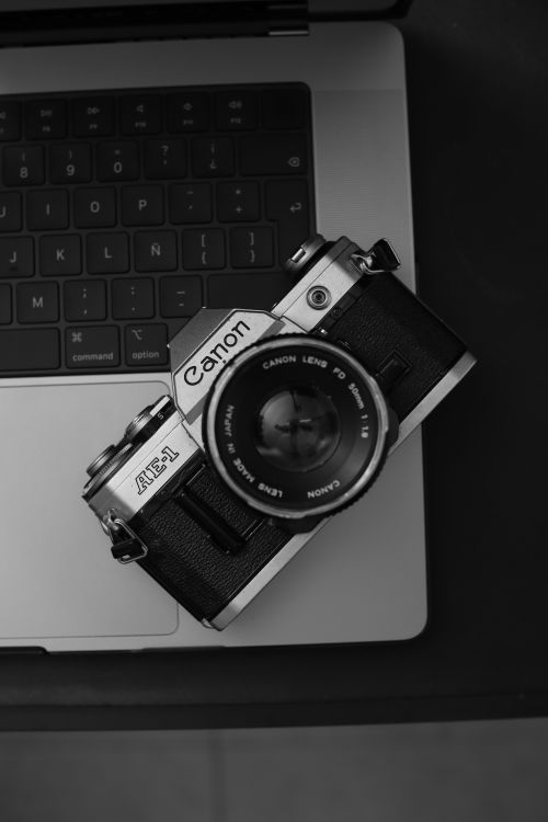 Free Monochrome image of a vintage Canon AE-1 camera resting on a laptop keyboard. Stock Photo