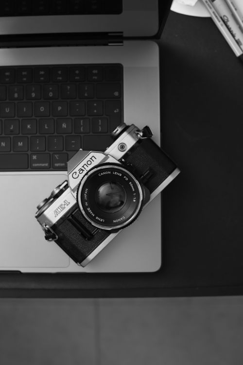 Free Vintage Canon AE-1 camera resting on a laptop, showcasing analog nostalgia and modern technology contrast. Stock Photo