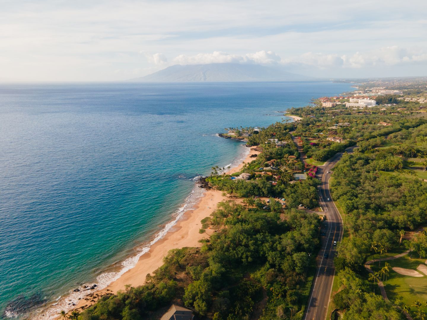 Coastal highway curving along a green Hawaiian shoreline seen from above