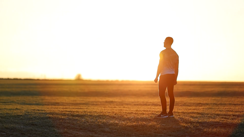 A silhouetted man stands in a sunlit field, embracing the early morning light.