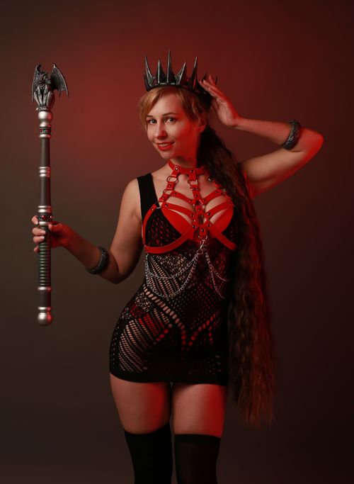 Free Woman in dramatic costume and crown posing with staff. Red background enhances her regal fantasy look. Stock Photo