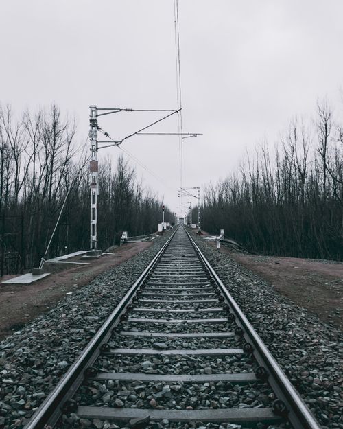 Free A solitary railway track stretching into the distance under an overcast sky with bare trees lining the way. Stock Photo