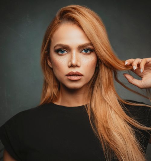 Free Close-up portrait of a woman with blonde hair and freckles against a gray studio background. Stock Photo