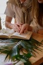 Woman Wearing a Book with a Girl while Sitting at a Table with Palm Leaves