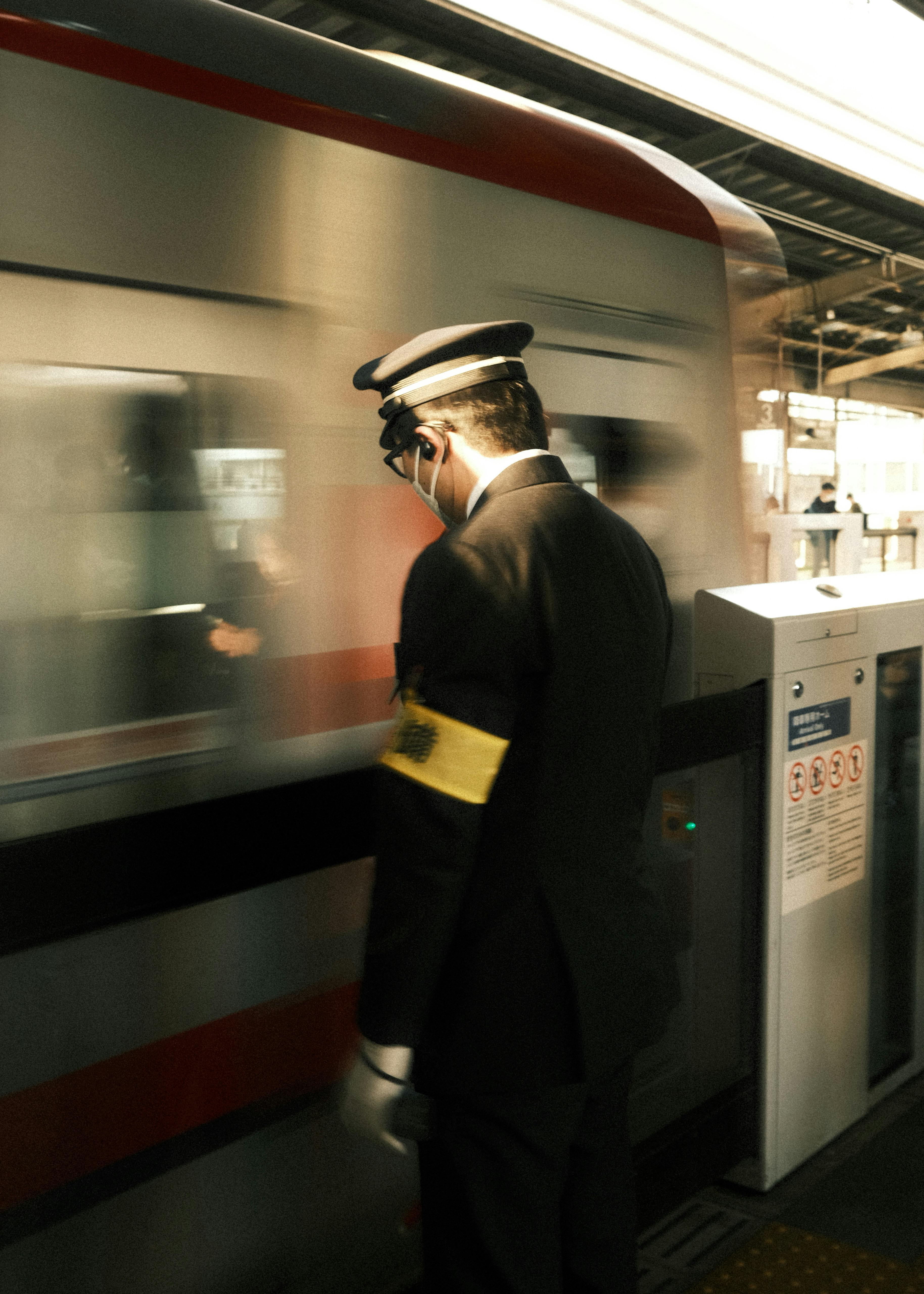 Guard in uniform stands at Tokyo station as a train passes by, capturing the essence of urban transportation.