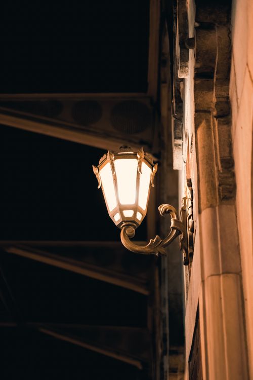 Free A close-up of a vintage street lamp illuminating a stone wall at night, exuding classic charm. Stock Photo