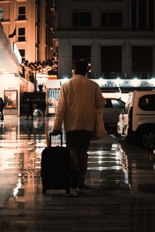Free A person with a suitcase walking on a wet sidewalk in a city at night. Stock Photo