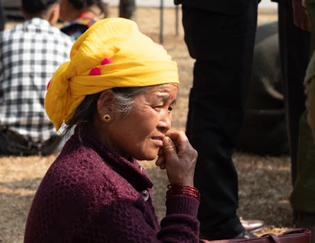 Elderly woman wearing a yellow turban, sitting outdoors in Pokhara, Nepal. Captured candidly in a park setting.