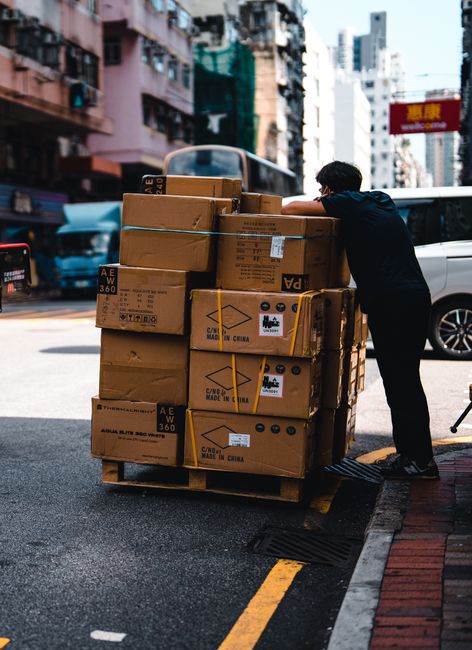 Man handling stacked boxes on a pallet in busy urban street scene. Man handling stacked boxes on a pallet in busy urban street scene.