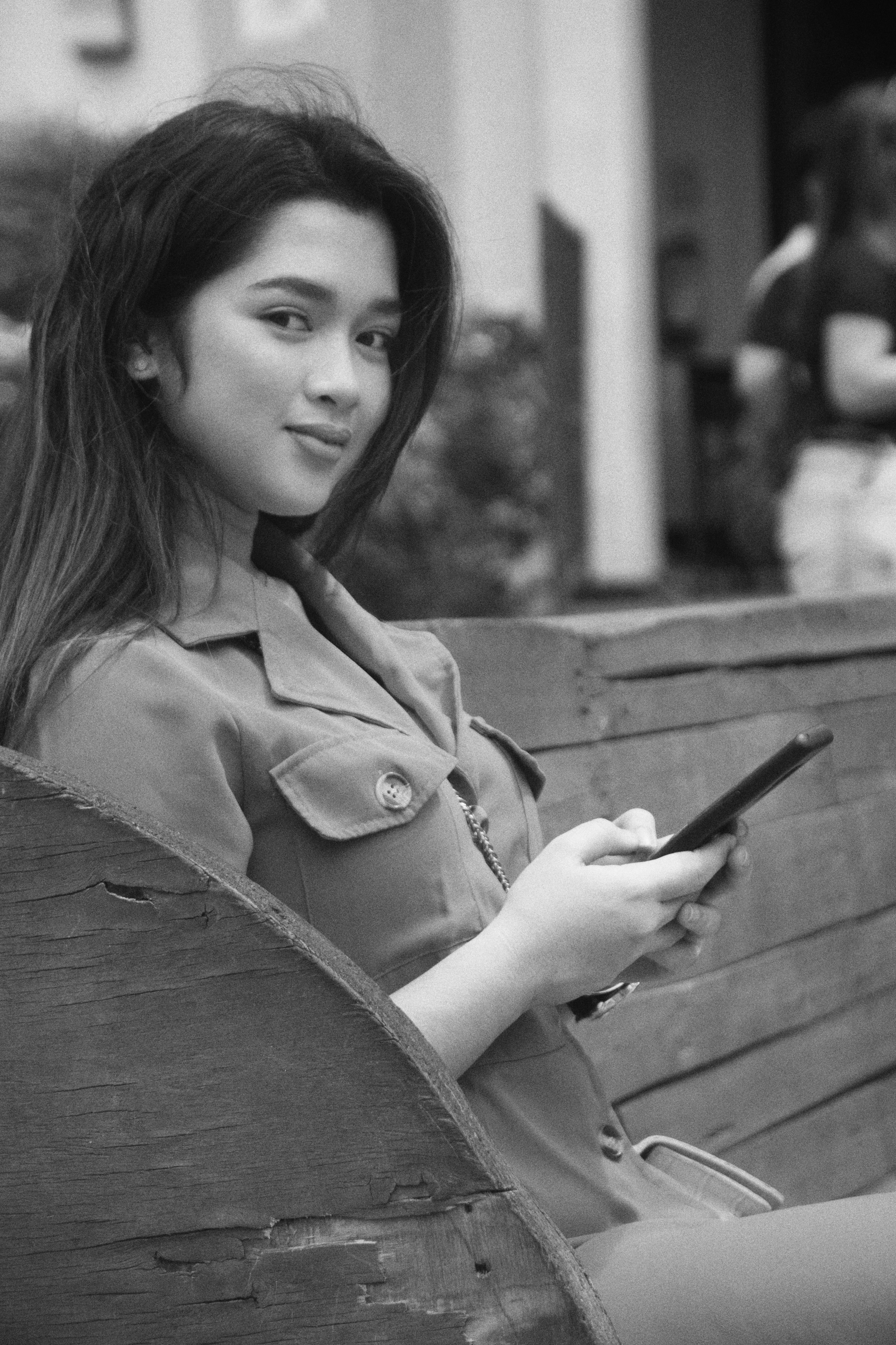Smiling young woman sitting on a bench using her smartphone outdoors in an urban setting.