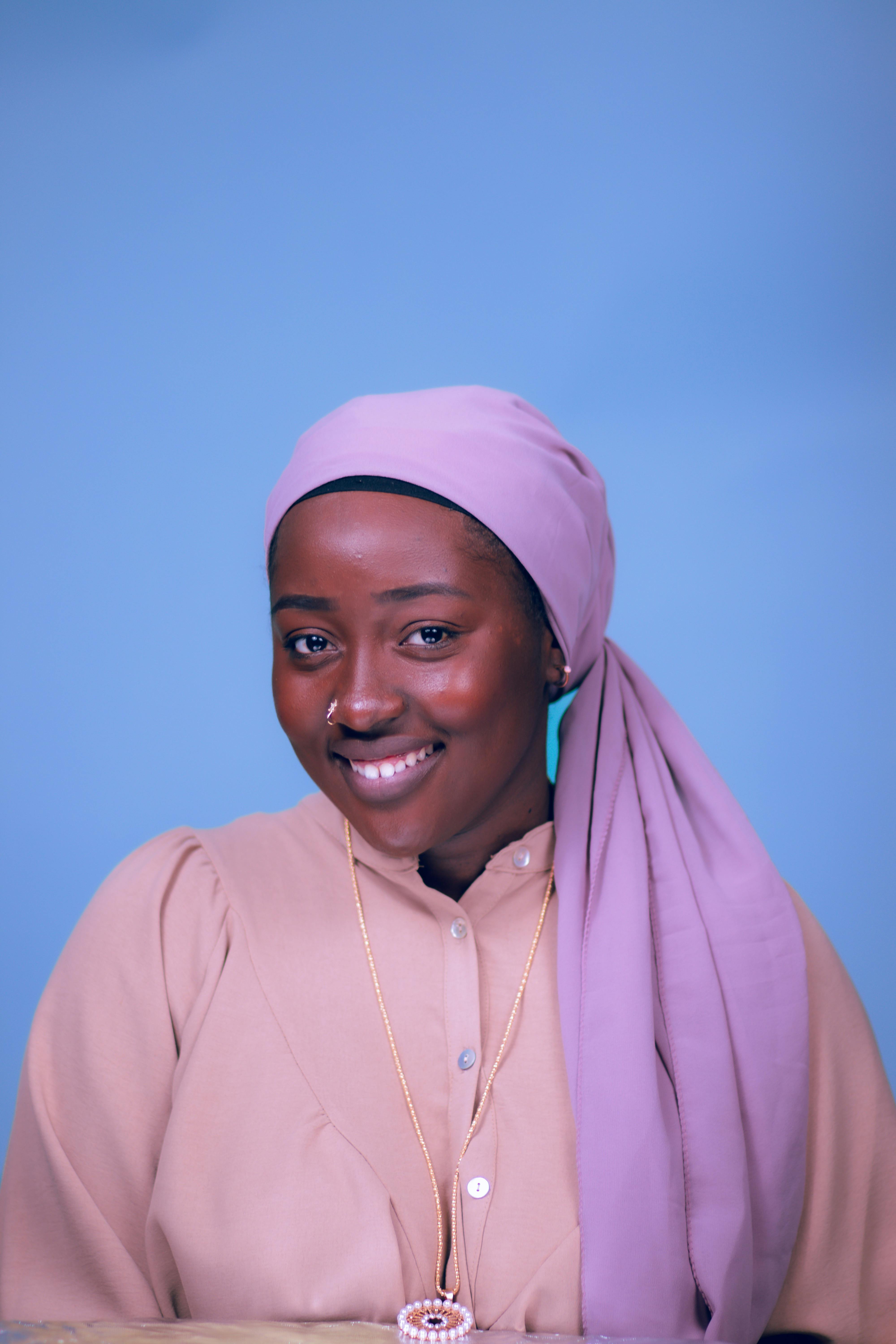 A vibrant portrait of a smiling woman in a traditional headscarf and pink outfit against a blue backdrop.