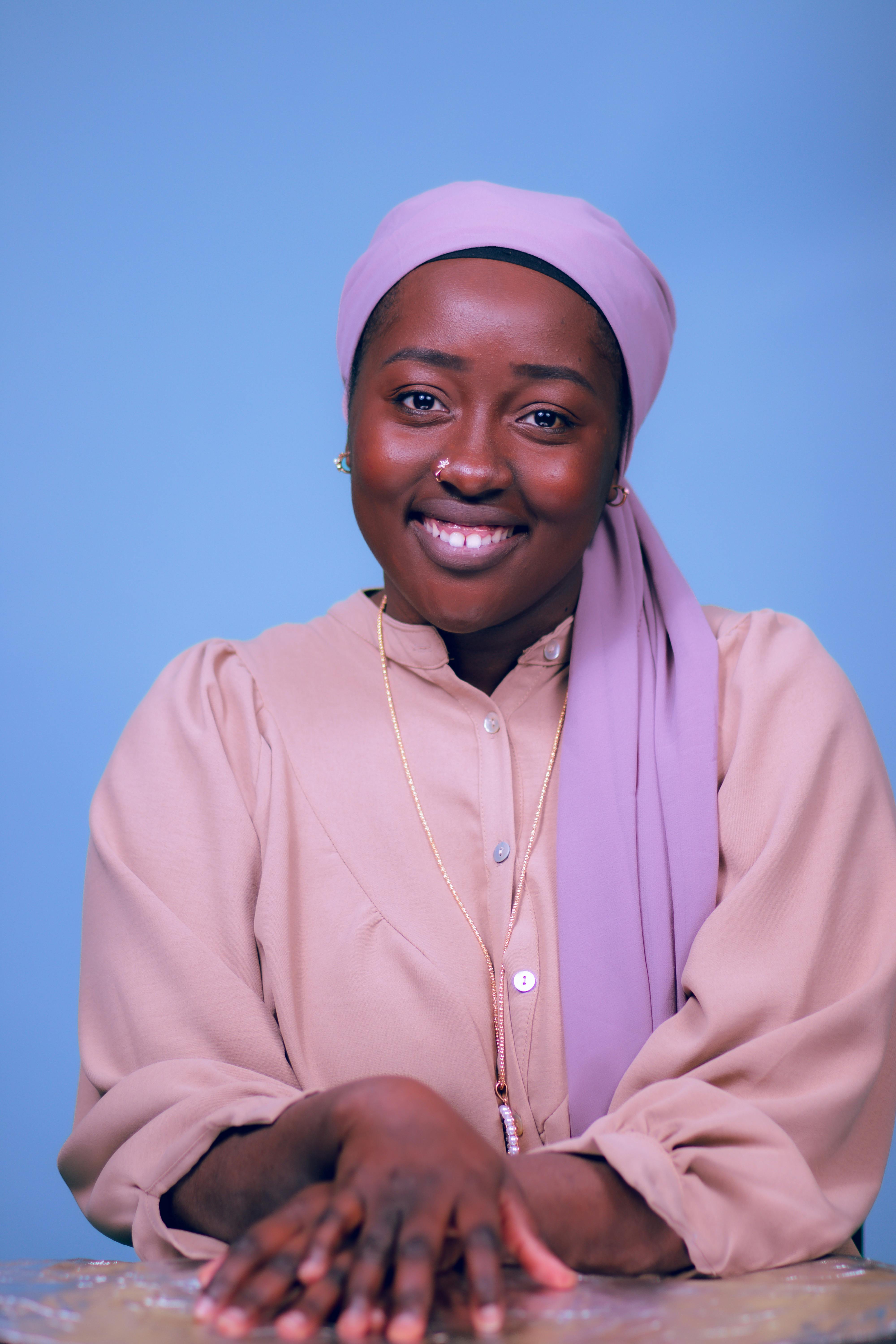 Portrait of a smiling woman with a headscarf against a blue background, exuding warmth and elegance.