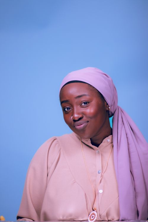 Free A young woman wearing a pink headscarf poses confidently against a blue background. Stock Photo