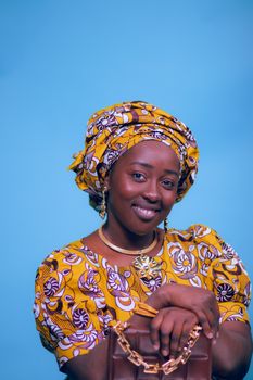 Smiling woman in colorful traditional attire posing in studio with blue background.