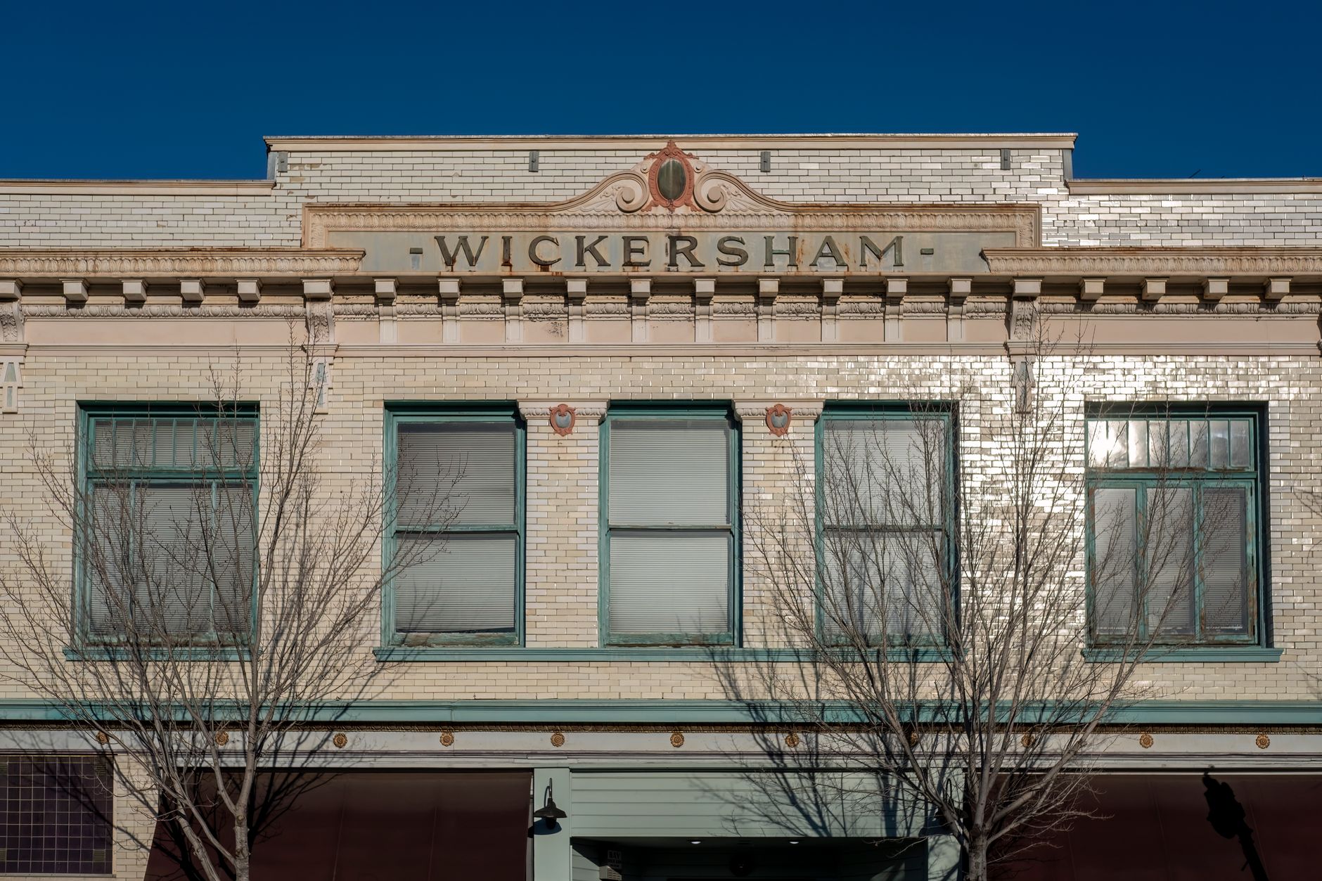 A detailed view of the Wickersham building facade with bare trees and clear blue sky.